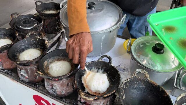 The process of making traditional dessert named Serabi made from rice flour and coconut milk by an old man with charcoal stove