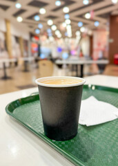 Paper glass of coffee on a table in a cafe with blurred bokeh