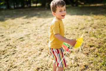 A happy 3-4 year old boy runs on the grass in the summer with a colorful pinwheel. Carefree...