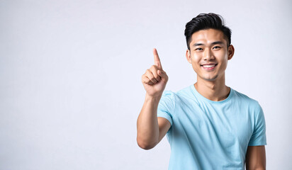 Fototapeta premium a smiling young man in a blue shirt is pointing upwards, asian male, pointing index finger, isolated white background, website banner, copy space, background