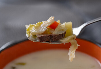 Spoon with vegetable soup and pieces of meat.