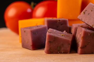 tomatoes, yellow cheese and diced lavender cheese on a cutting board.