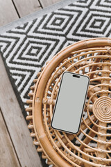 Mobile phone with blank screen on ornamental bamboo table and carpet. Flat lay, top view mock up with copy space. Bohemian, coastal, organic modern and tropical style - 784319229