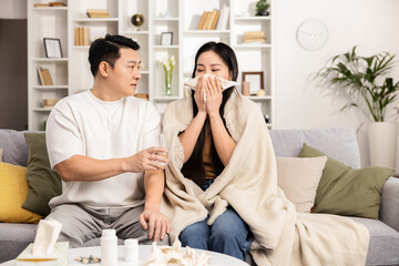 A caring scene of a couple as one comforts the other who is feeling unwell, wrapped in a blanket at home.