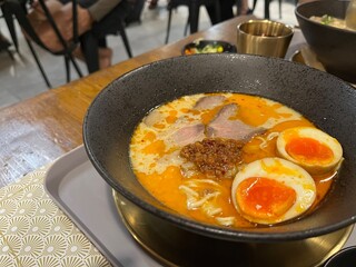 A bowl of Japanese Tonkotsu Ramen with egg, smoked beef and spicy creamy broth. Served with green tea and some garnish