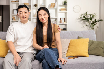 An Asian couple engages in online shopping and financial planning using a tablet and smartphone, having a call with family while comfortable at home.