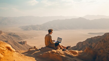 Man with laptop sitting on top of a mountain.