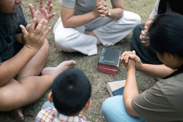 Young woman held her mother's hand in prayer, surrounded by their outdoor community, where love and family life flourished through shared moments of prayer and support. Group christian pray concept.