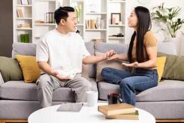 A peaceful couple sits on a couch practicing mindfulness meditation together, creating a serene atmosphere in a well-lit living room.