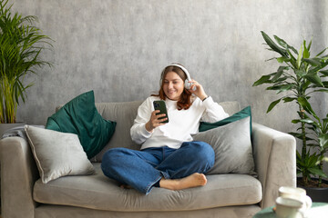 Smiling girl relaxing at home, she is listening to music, using a smartphone and wearing white...