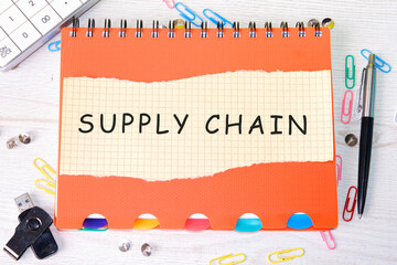 The words Supply Chain written on a piece of paper on an orange notebook