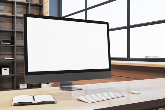 Close up of clean designer office workplace with empty white computer monitor, window with city view and wooden shelves in the background. Mock up, 3D Rendering.