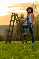 a woman in dungarees with a ladder on a meadow