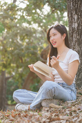 Young asian women sitting on grass under the tree to writing business data and journey dairy in notebook while enjoying and happiness to relaxation with journey travel lifestyle in the nature park - 784337406