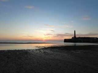 Pink sunset shining behind the calm sea and the silhouette of a lighthouse