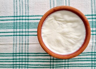 Top view of Bulgarian yoghurt in a clay bowl on the table covered with a flannel tablecloth - obrazy, fototapety, plakaty