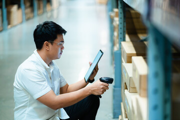 A man is looking at a tablet while holding a barcode scanner. He is in a warehouse and he is...