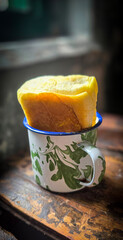 Ice chocolate drink on a vintage Indonesian iron mug with random green pattern called Blirik cup or cangkir Blirik on bokeh background along with chocolate filling bread