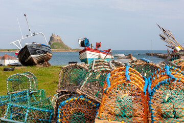 Lindisfarne, Holy Island, Northumberland, UK: the castle and harbour from the Common, with traditional old fishing boats and lobster pots in the foreground.