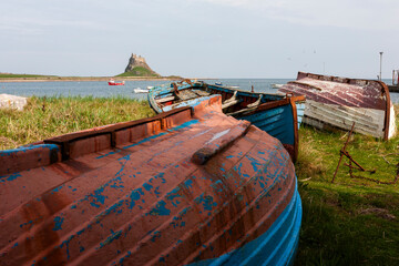 Lindisfarne, Holy Island, Northumberland, UK: traditional old fishing boats in the foreground, and the castle and harbour beyond