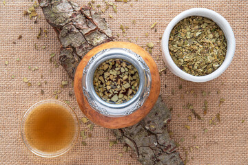 Mate tea in a typical South American calabash, with dried leaves next to it - 784350212