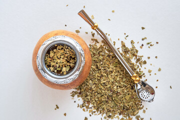 Mate tea in a typical South American calabash, with dried leaves next to it - 784350264