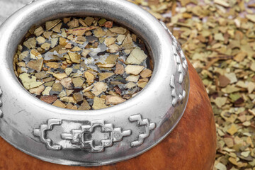 Mate tea in a typical South American calabash, with dried leaves next to it - 784350280