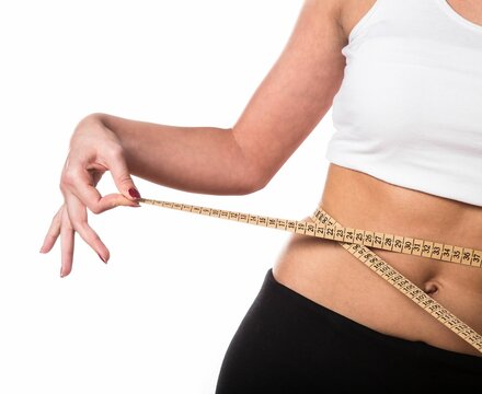 Woman in a white crop top wrapping a tape measure around her waist to show weight loss