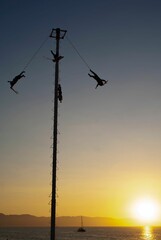 Silhouette of people enjoying Voladores de Papantla (flying men)  at sunset with a seascape view