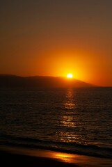 Red sunset view over a seascape with clear sky and sun in the background stones silhouettes around