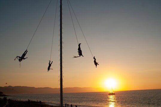Silhouette of people enjoying Voladores de Papantla (flying men)  at sunset with a seascape view