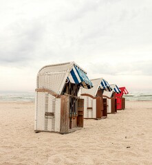 Row of four wicker beach chairs on a sandy beach under cloudy sky