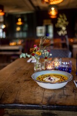 Vertical shot of Pumpkin soup served in a bowl on a wooden table in a cafe
