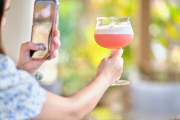 Female taking pictures of her pink cocktail in the outdoor bar