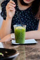 Vertical shot of a female drinking a green juice with lemon and ice