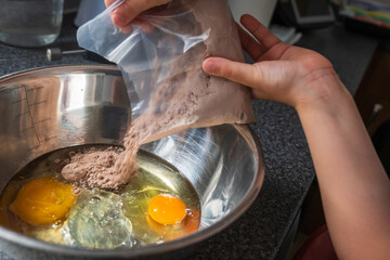 Child hands adding cupcake mix powder to a mixer bowl to make a dessert dough