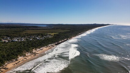 Aerial view of lake waves breaking greenery beach with buildings in New South Wales