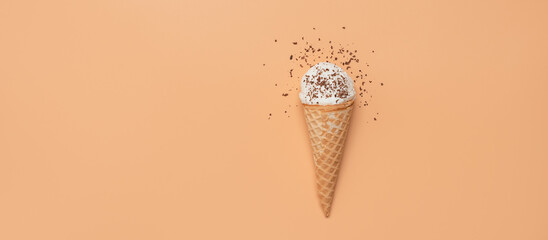 Ice cream in a waffle cone with chocolate chips on a pastel peach background. Top view, flat lay, selective focus. Banner