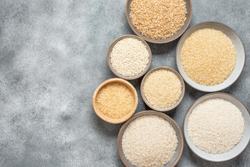 Various raw dry rice in bowls on gray background. View from above.