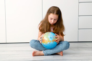 a little cute girl sitting on the floor carefully examines the globe