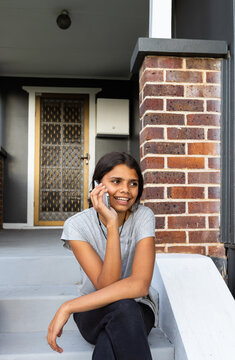 teenaged aboriginal girl sitting on porch steps talking on mobile phone