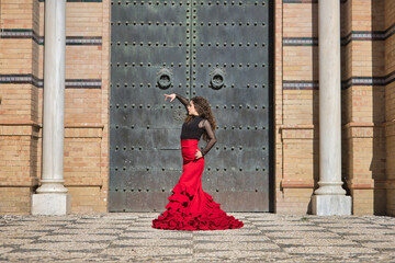 Young, beautiful, brunette woman in black shirt and red skirt, dancing flamenco in front of an old, black metal door. Flamenco concept, dance, art, typical Spanish.