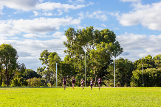 five children running away towards goal posts on football oval