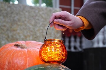 a woman's hand holds a close-up orange glass basket in the form of a pumpkin with a glowing garland...