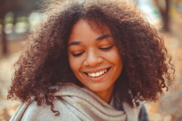 Cute autumn portrait of young happy curly african american woman enjoying fall season in park