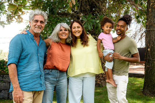 Happy diverse multigenerational family embracing in a sunny garden, a portrait of authentic love and togetherness showing grandparents with children and grandchild.