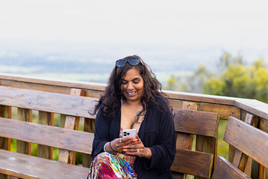 woman sitting on parkbench in scenic location looking at mobile phone