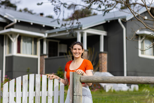 young female homeowner standing smiling at the gate of her home