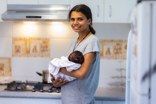 teen girl cradling baby sister in kitchen at home