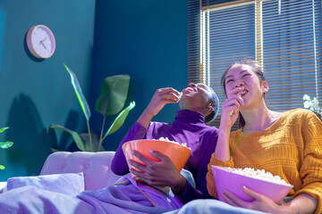 Cheerful friends watching comedy movie laughing eating popcorn at home at night. High quality photo